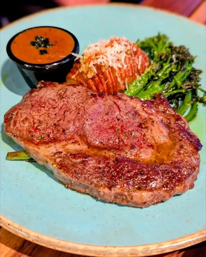 A grilled steak with hasselback potato, charred greens and pepper sauce