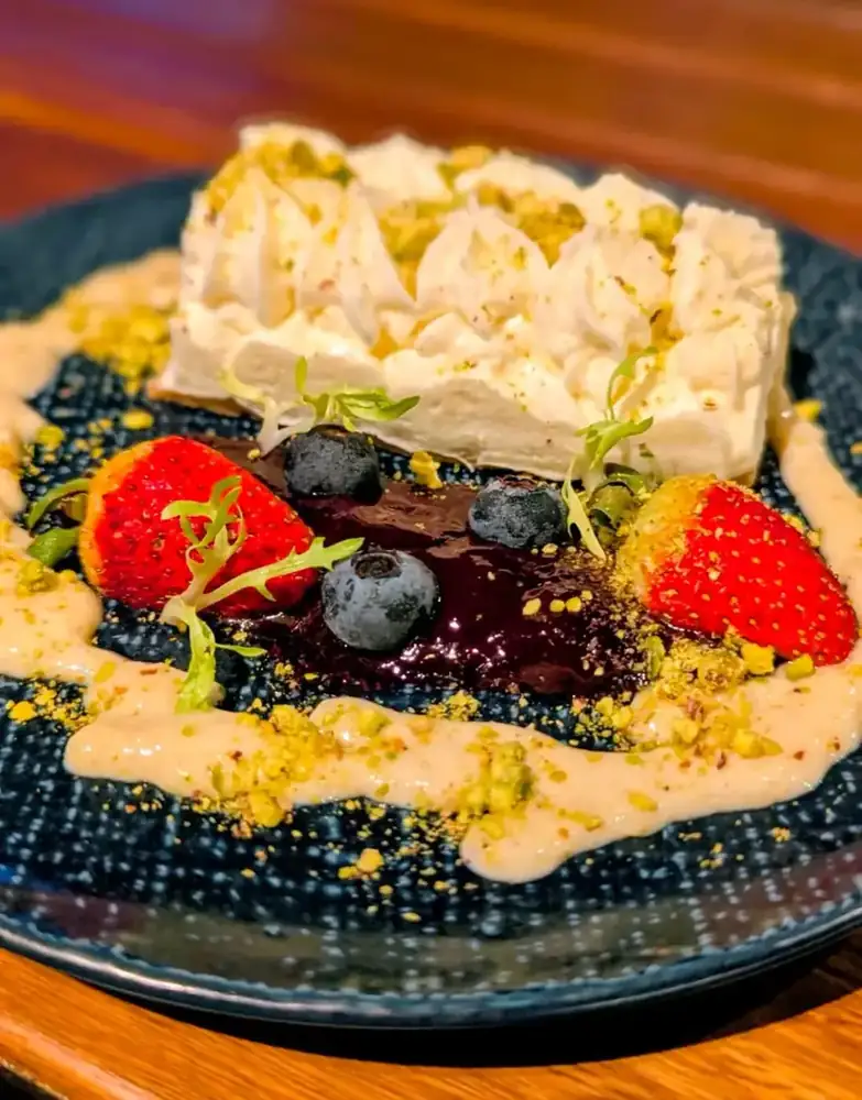 A plated dessert with citrus cream, berries and crumb