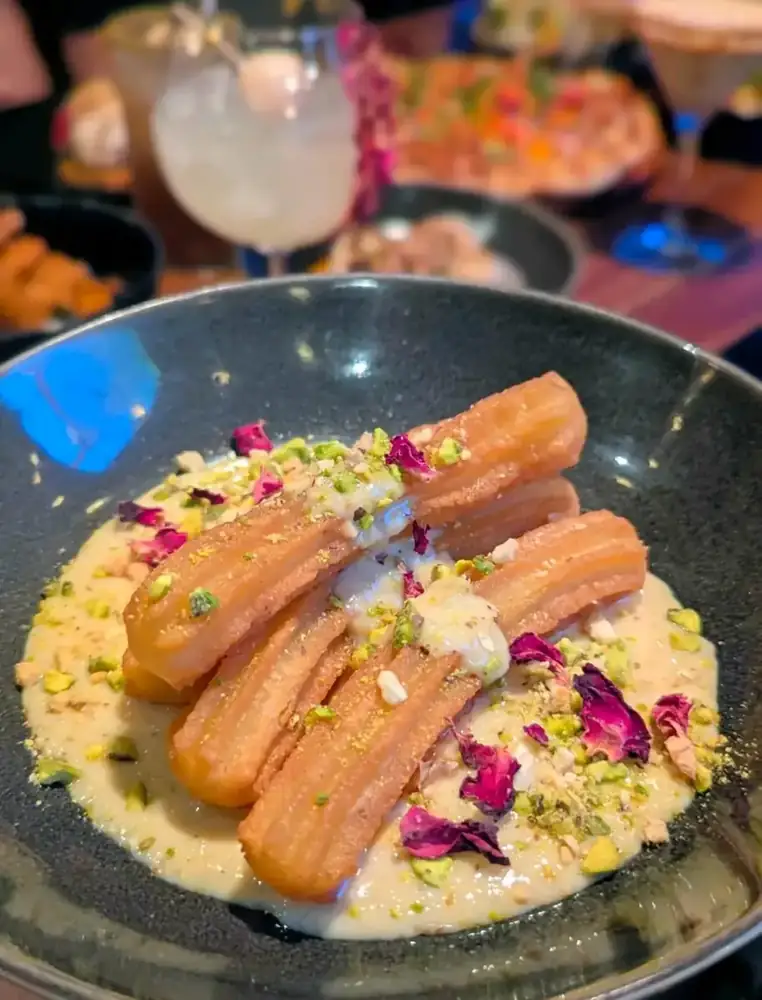 Churros with pistachio and dried rose on a creamy sauce