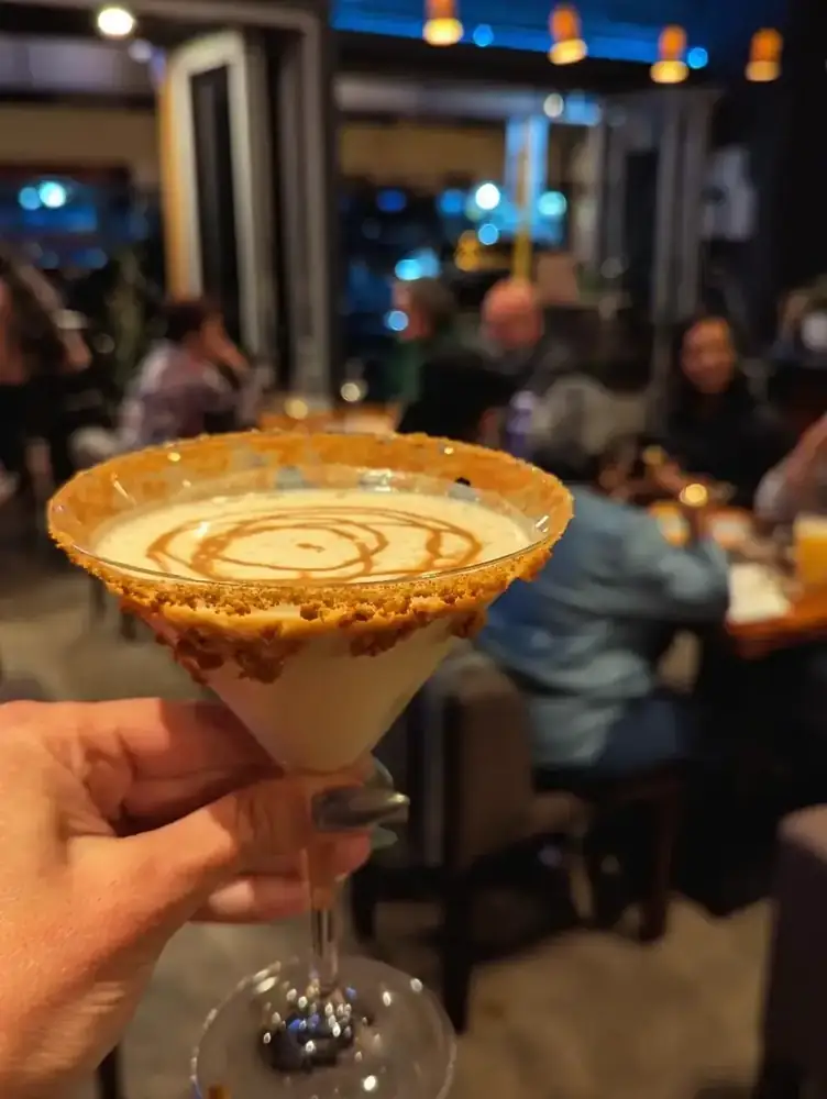 A Biscoff martini with a biscuit crumb rim, held up in the dining room