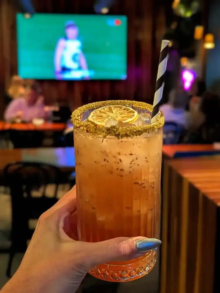 A tall iced tea cocktail with a lemon wheel, held up at the bar