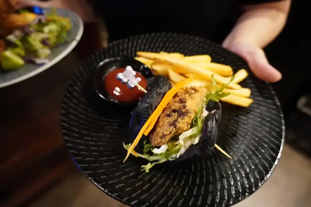 A burger with chips and dipping sauce on a dark plate