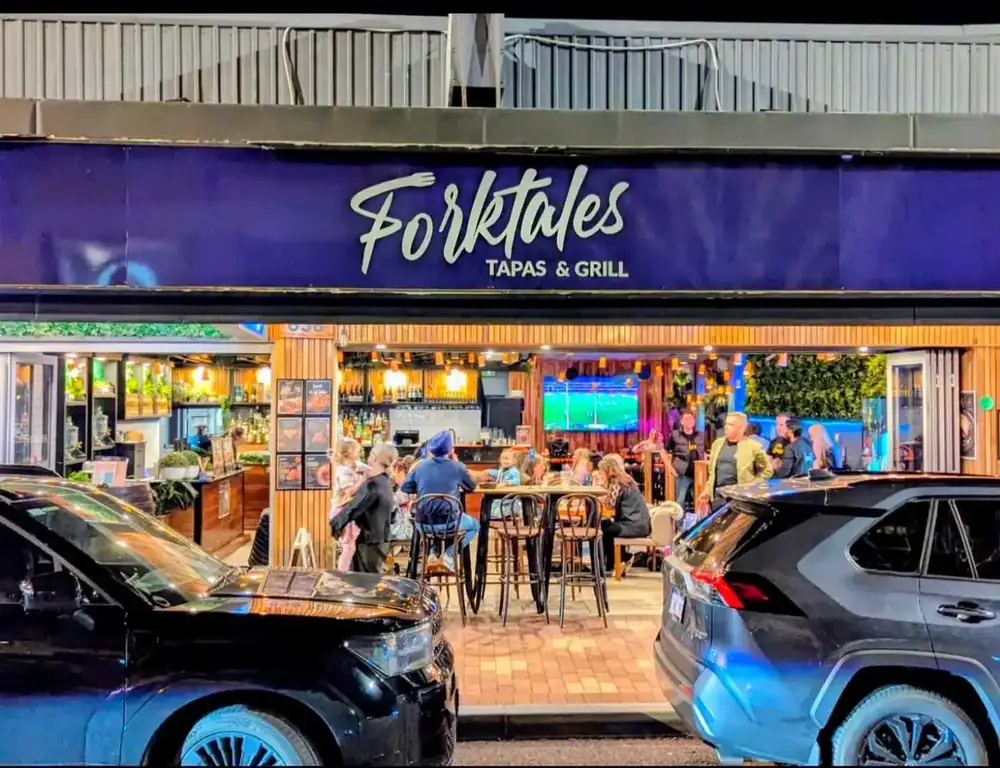 The Forktales shopfront lit up at night, seen from Beaufort Street