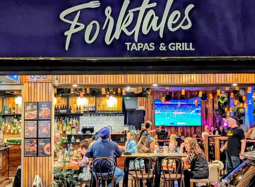 The lit Forktales sign above the entrance at night, with guests inside