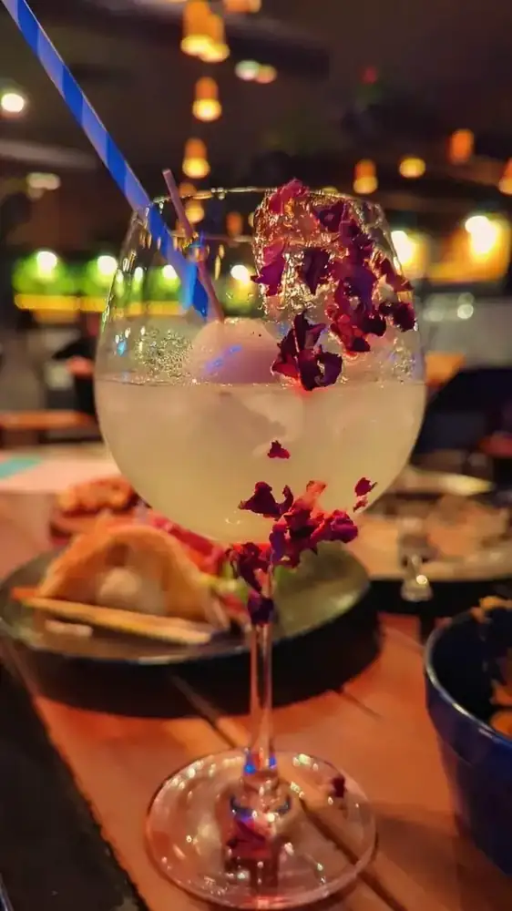 A cocktail garnished with rose petals on the bar