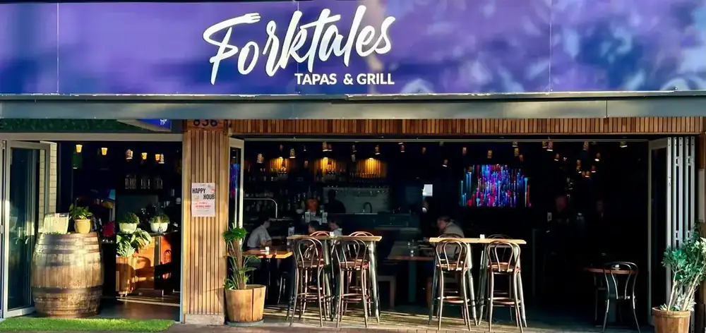 Forktales at night with the sign lit above the open frontage