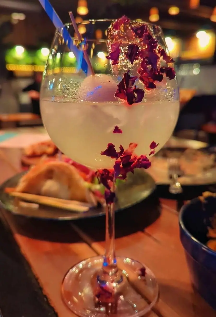 A gin cocktail with lychee and dried rose petals on a table at Forktales